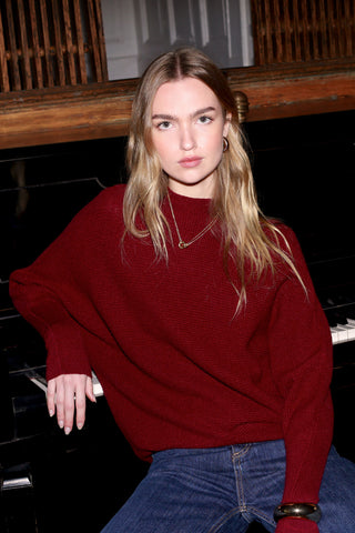 Woman in a red sweater sitting on a piano in a room with wooden walls.