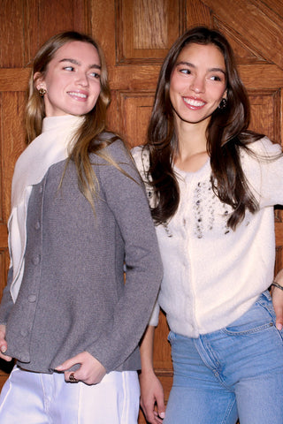 Two women posing together against a wooden paneled wall.