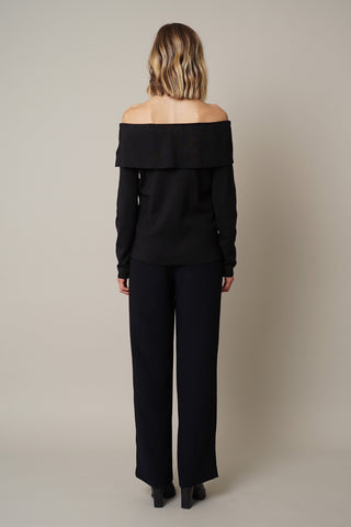 A woman wearing a black off-the-shoulder Marilyn Sweater with Stones from Cyrus and wide leg trousers.